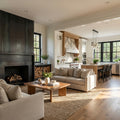A bright, modern open-concept living room with a large dark wood fireplace, beige sofas, a wooden coffee table, and a woven area rug, with a kitchen visible in the background. floor plan to render ai
